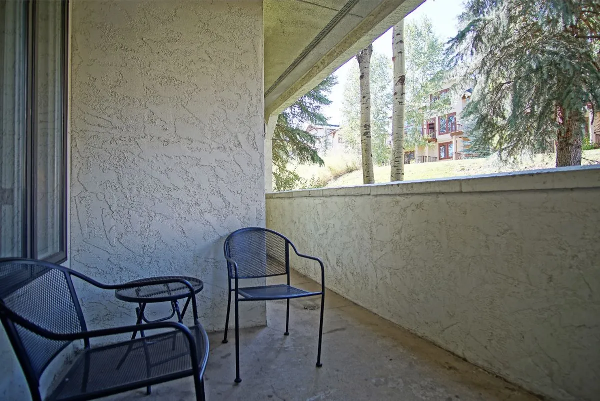 A serene balcony or patio overlooking natural surroundings, furnished with two black metal chairs and a small round table. The view invites moments of relaxation, morning coffee, or unwinding after a day out.