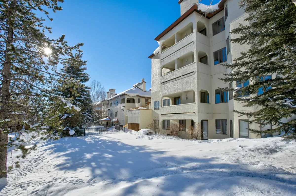 A wide exterior view of multi-story buildings nestled in a picturesque, snow-covered landscape. Trees dusted with fresh snow line the surroundings, evoking the excitement of a ski town in winter.