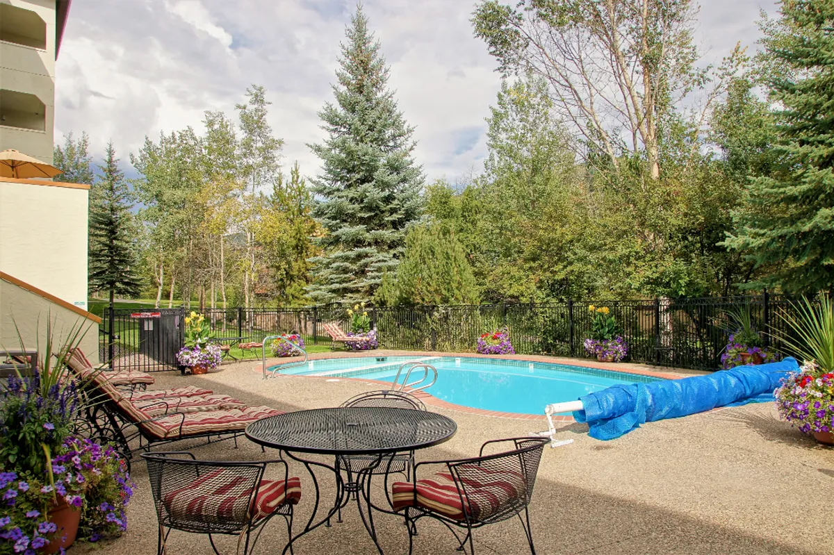 An inviting outdoor swimming pool bordered by comfortable seating areas, lush greenery, and colorful decorative flowers. The setting feels tranquil and perfect for both daytime relaxation and evening gatherings. The pool is positioned to take advantage of the natural surroundings, providing a resort-like ambiance.