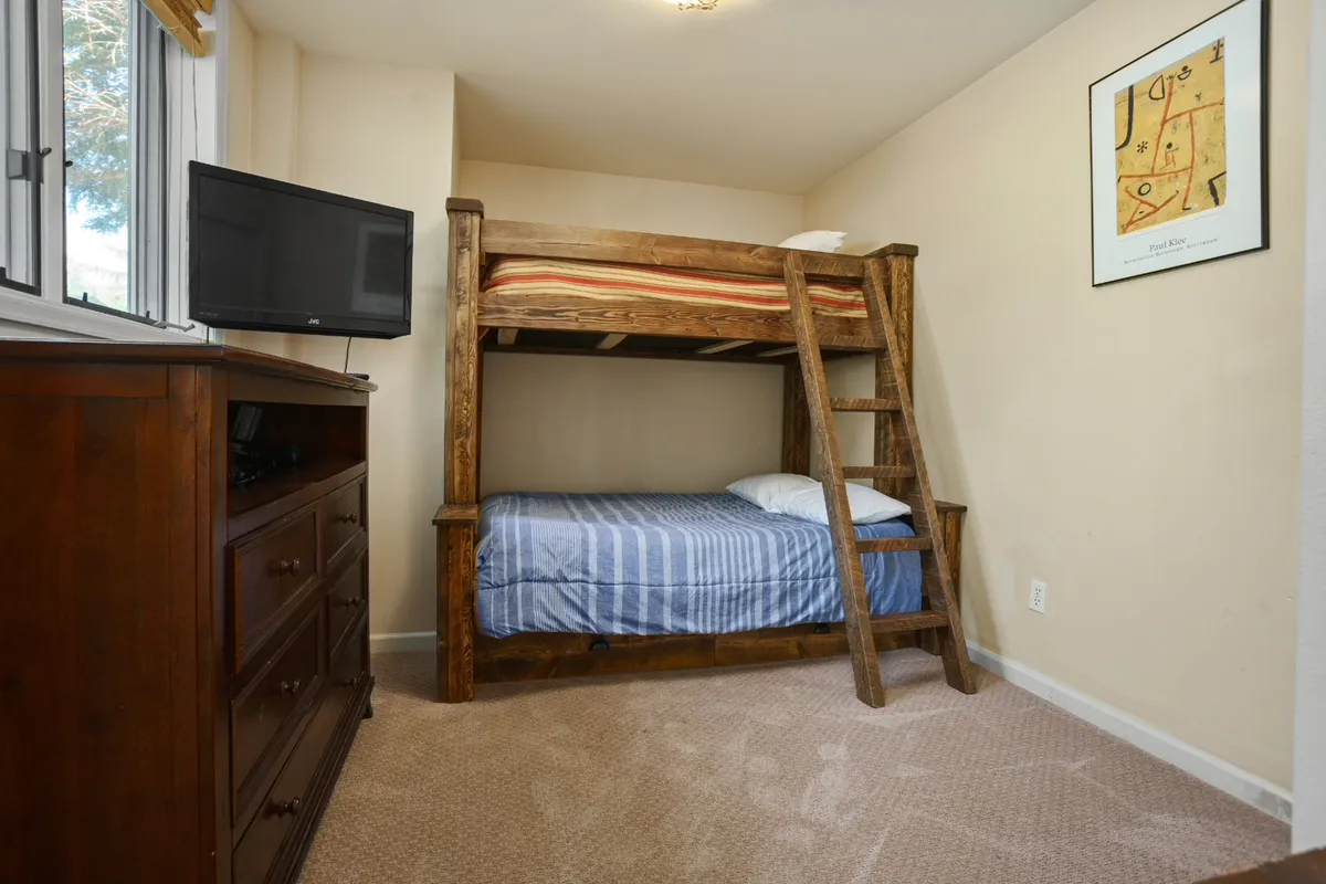 A bright, cheerful second bedroom equipped with a bunk bed, a dresser, and a wall-mounted television. The space is designed for flexibility and fun, encouraging story times, group stays, and a sense of adventure for kids or families.