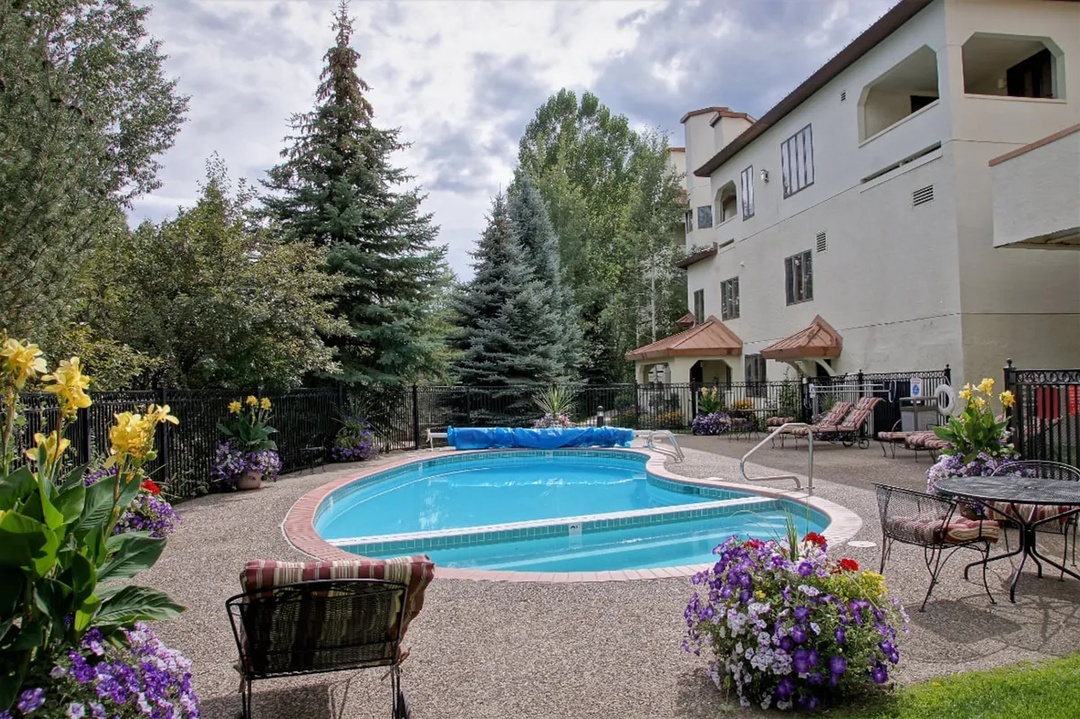 An inviting outdoor swimming pool surrounded by colorful flower beds, lounge chairs, and the building's facade, set under bright sunlight—ideal for group relaxation after a day of adventure.