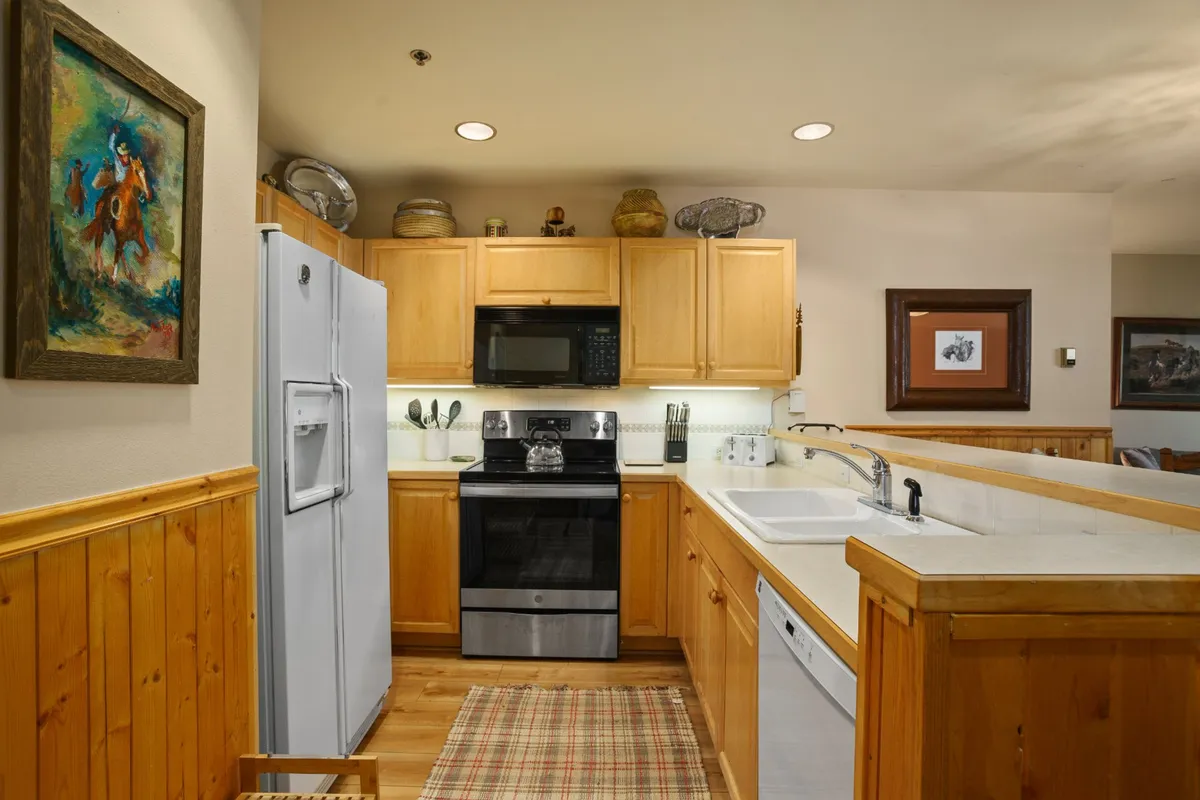 A bright and welcoming kitchen featuring modern stainless steel appliances, wooden cabinetry, and a decorative rug. The space is designed for both cooking and socializing, making it perfect for preparing meals before or after outdoor excursions throughout the year.