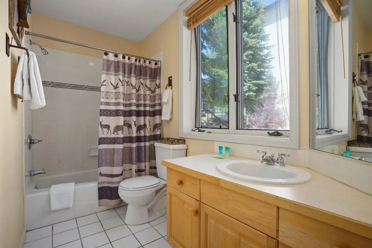 A calming bathroom with a wooden vanity, large window, and a shower with a patterned curtain. Natural light fills the space, offering a sense of tranquility and self-care, perfect for unwinding after a day of adventure.