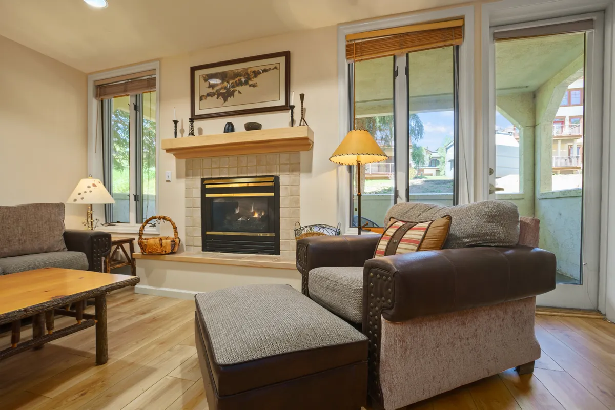 A welcoming living room with a fireplace, a comfortable seating area, and large windows that draw in natural light. The space feels warm and inviting, perfect for relaxing after a day spent exploring the mountains or enjoying après-ski. Subtle décor and a coffee table create an atmosphere ideal for gathering with friends or family.