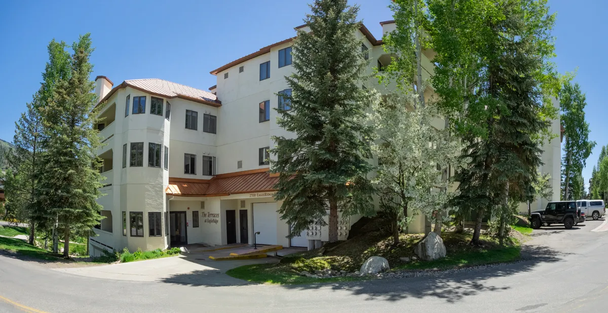 This image features the building's welcoming facade framed by lush trees, with the entrance area visible. The environment looks inviting, suggesting easy access and a prime location close to nature and local amenities.