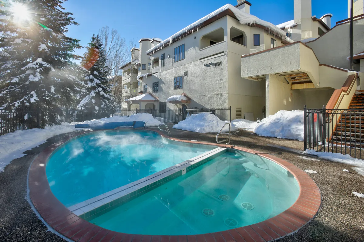 An exterior shot of a swimming pool surrounded by snow, with distinctive building architecture in the background. The image captures the unique opportunity for year-round fun—swimming or relaxing poolside even in winter conditions.