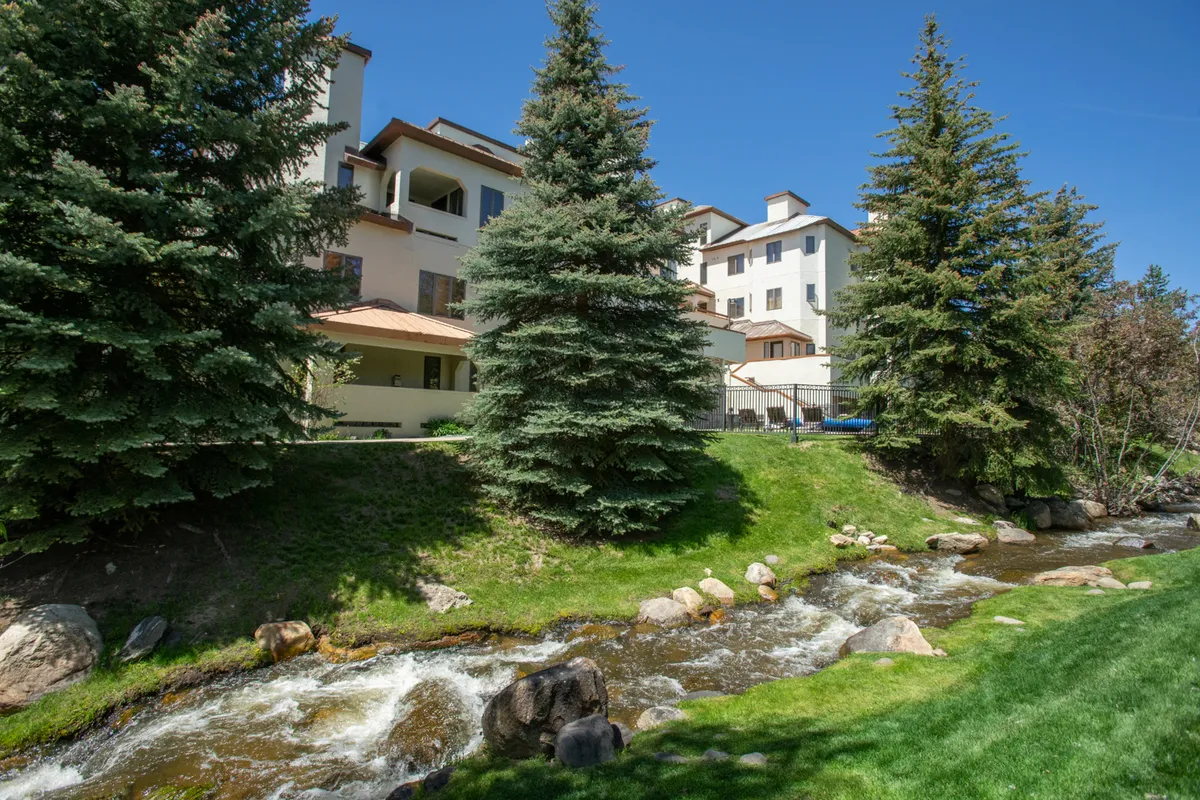 A tranquil exterior view highlighting the private patio with a backdrop of a flowing creek and lush greenery. The setting invites both quiet morning coffees and post-adventure relaxation, directly connecting indoor comfort with outdoor beauty.